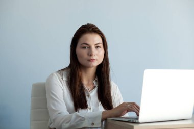 Ofis elbiseli genç ve güzel bir kız dizüstü bilgisayarla çalışıyor.