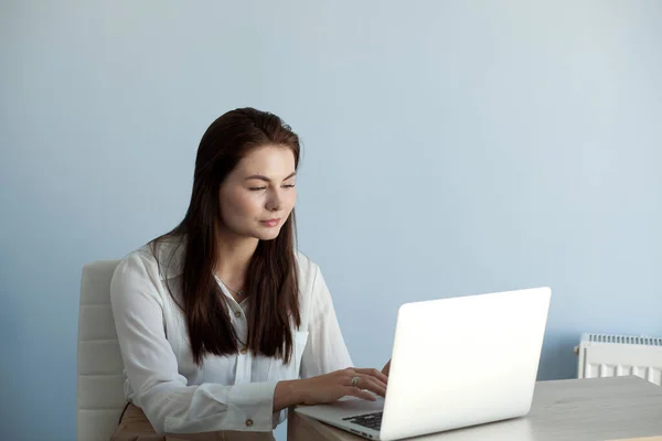 Ofis elbiseli genç ve güzel bir kız dizüstü bilgisayarla çalışıyor.