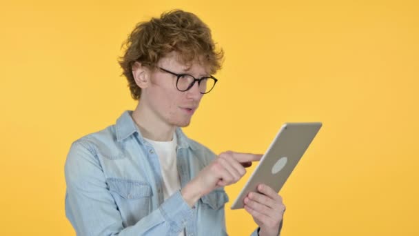 Рыжий молодой человек празднует на планшете, желтый фон — стоковое видео