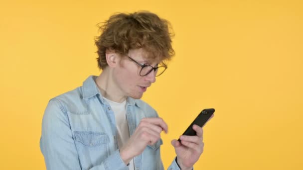 Pelirroja joven celebrando en Smartphone, fondo amarillo — Vídeos de Stock