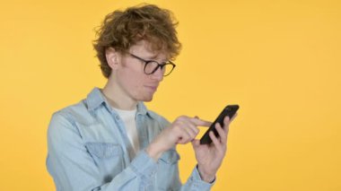 Kızıl saçlı genç adam akıllı telefon kullanıyor, sarı arkaplan 
