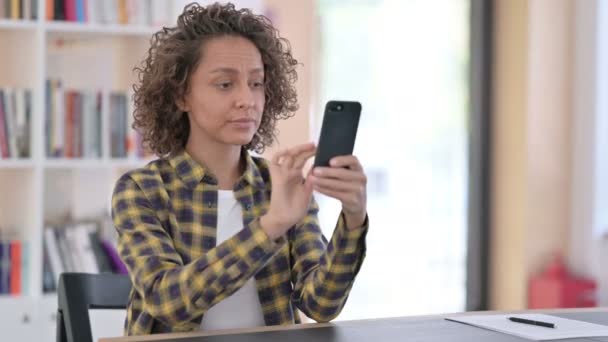 Mujer de raza mixta infeliz con pérdida en el teléfono inteligente en el trabajo — Vídeos de Stock