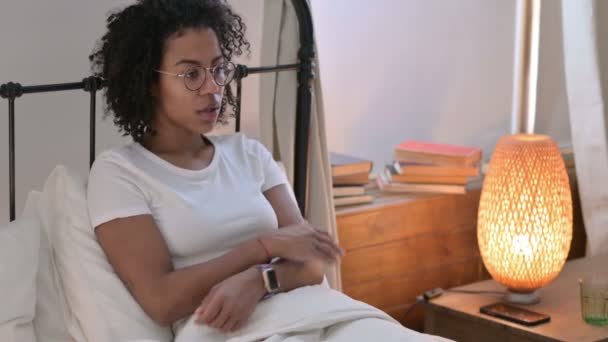 Больная молодая африканская женщина чихает сидя в постели — стоковое видео