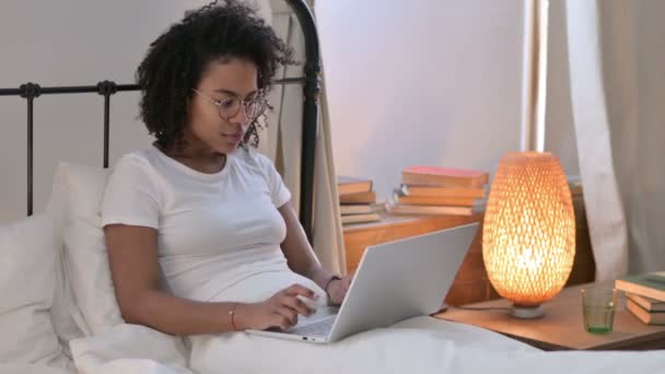 Atractiva joven africana celebrando en el ordenador portátil en la cama — Vídeo de stock
