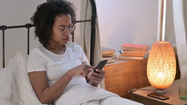 Fracaso, Mujer Africana joven reaccionando a la pérdida en el teléfono inteligente en la cama — Vídeos de Stock