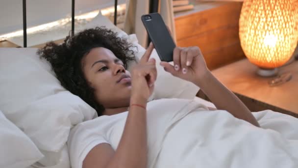 침대에 누워 있는 젊은 아프리카 여자가 사용하는 스마트폰 — 비디오