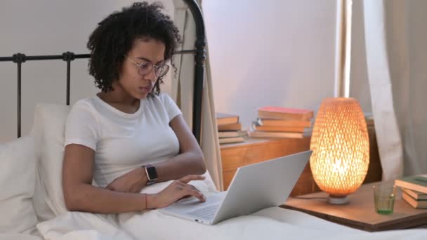 Mujer joven africana con ordenador portátil pensando en la cama — Vídeos de Stock