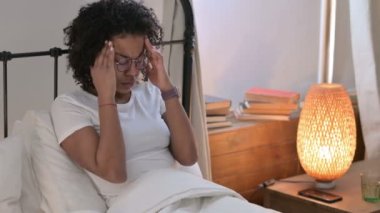 Yatakta oturan baş ağrısı olan genç Afrikalı kadın. 