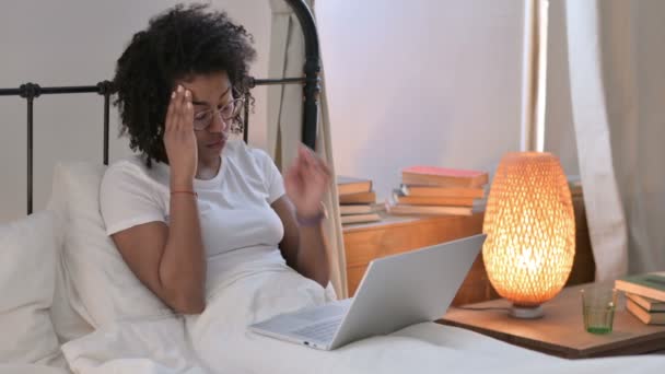 Joven mujer africana con portátil con dolor de cabeza en la cama — Vídeo de stock