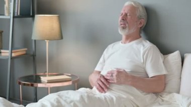 Yaşlı adam göğüs ağrısı çekiyor. Yatakta oturuyor. 
