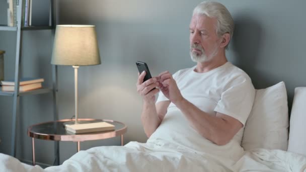 Utilisation du smartphone par le vieil homme âgé au lit — Video