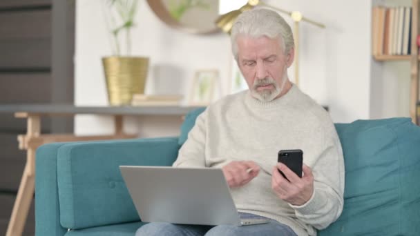 Senior Old Man που εργάζονται σε Smartphone και Laptop στον καναπέ — Αρχείο Βίντεο