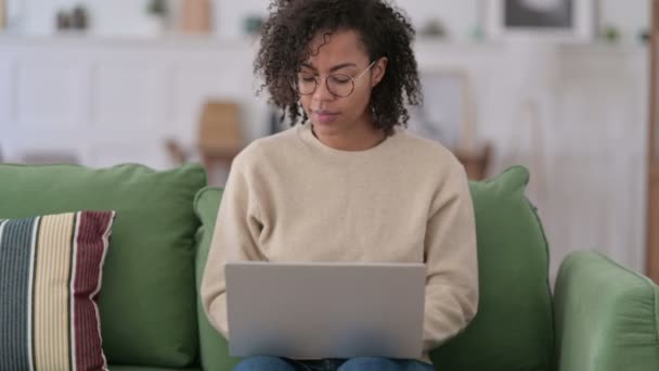 Éxito joven africana con el ordenador portátil celebrando en el sofá — Vídeo de stock