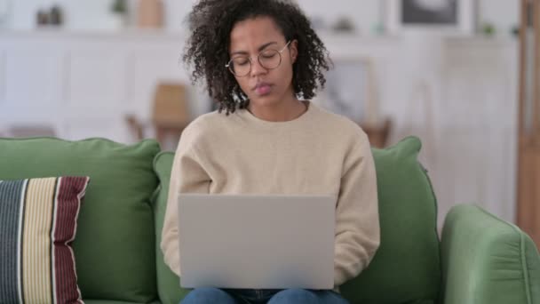 Jeune femme africaine avec ordinateur portable ayant la douleur au poignet sur le canapé — Video