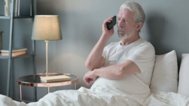 Yaşlı adam yatakta Smartphone 'da konuşuyor. 