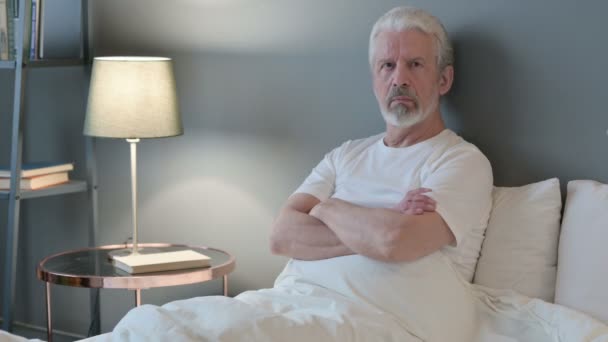 Ernsthafter alter Mann blickt im Bett auf Kamera — Stockvideo