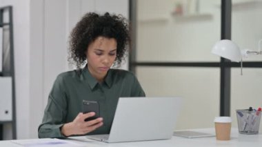 İş yerinde akıllı telefon kullanan dizüstü bilgisayarlı Afrikalı Kadın
