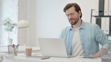 Sırt ağrısı olan genç adam laptopta çalışıyor. 