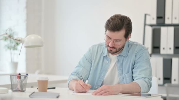 Jonge man die op papier schrijft op kantoor — Stockvideo