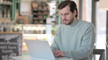 Laptoplu genç adam Cafe 'deki kameraya bakıyor. 