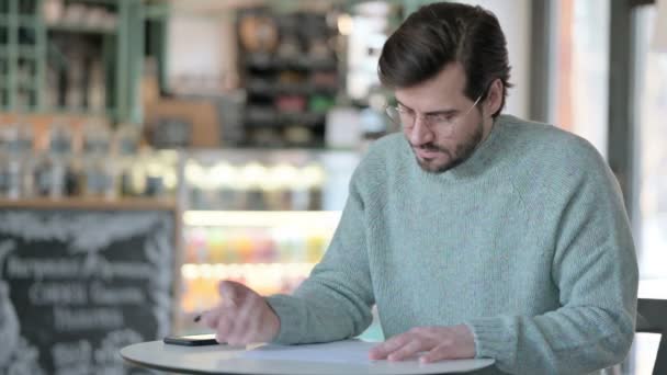 Junger Mann schreibt im Café auf Papier — Stockvideo