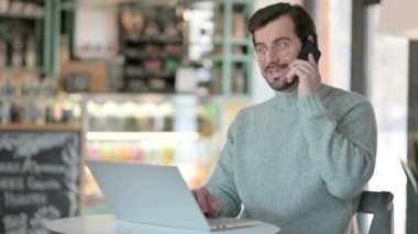 Dizüstü bilgisayarlı genç adam Smartphone 'da konuşuyor 