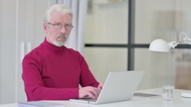 Dizüstü bilgisayar kullanırken kameraya bakan yaratıcı yaşlı adam