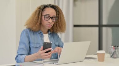 Ofiste akıllı telefon ve dizüstü bilgisayar üzerinde çalışan Afrikalı Kadın 