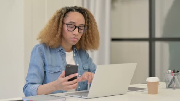 Ofiste akıllı telefon ve dizüstü bilgisayar üzerinde çalışan Afrikalı Kadın — Stok video