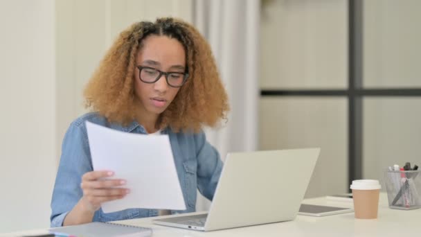 Afrikanerin liest Dokumente, während sie am Laptop arbeitet — Stockvideo