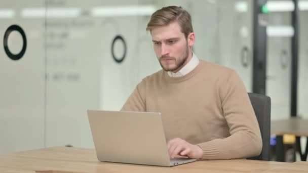 Δημιουργικός νεαρός άνδρας με φορητό υπολογιστή που έχει πόνο στην πλάτη στο γραφείο — Αρχείο Βίντεο