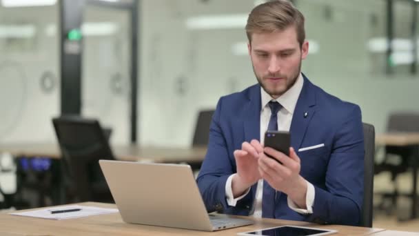 Бизнесмен с ноутбуком с помощью смартфона на работе — стоковое видео