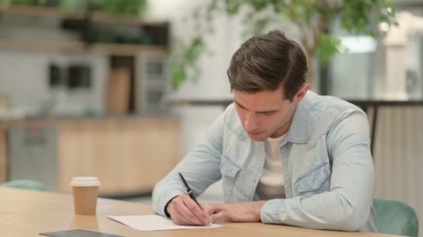 Kreativer junger Mann schreibt auf Papier und denkt nach — Stockvideo