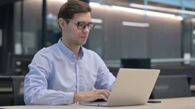 Başarılı genç adam iş yerinde dizüstü bilgisayarında kutlama yapıyor. 