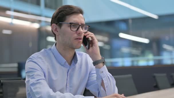 Молодой человек разговаривает по телефону на работе — стоковое видео