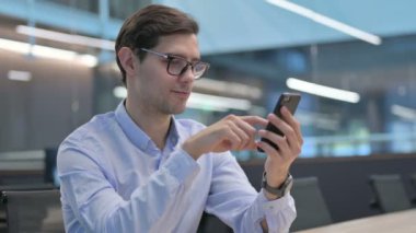 Genç adam iş yerinde akıllı telefon kullanıyor. 