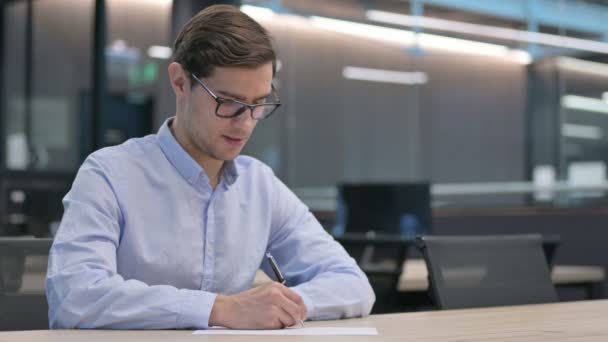Тяжелый молодой человек, пишущий на бумаге, думающий — стоковое видео