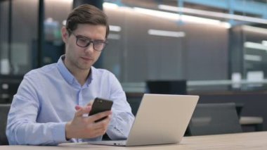 Akıllı telefon kullanan dizüstü bilgisayarı olan genç adam. 