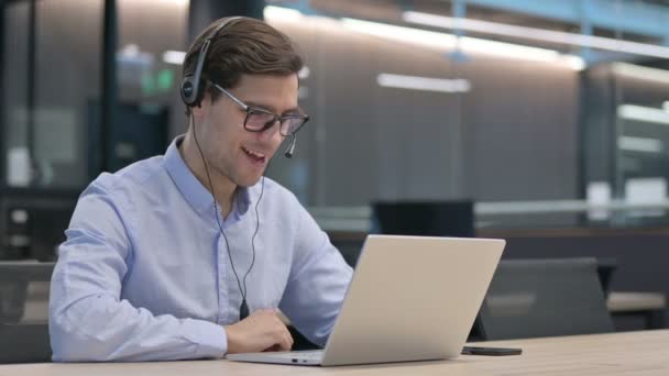 Kulaklıklı genç adam laptopta video çağrısı yapıyor. — Stok video