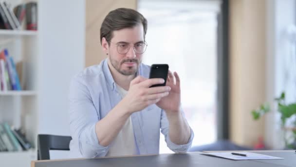 Hombre con gafas celebrando el éxito en el Smartphone en la oficina — Vídeos de Stock