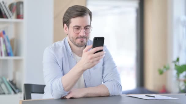 Hombre atractivo en gafas usando Smartphone en la oficina — Vídeos de Stock