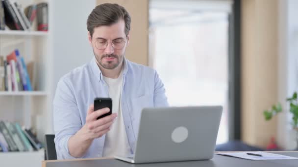 Hombre en gafas con portátil usando Smartphone en la oficina — Vídeo de stock