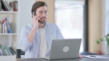Dizüstü bilgisayarlı Kızgın Adam Akıllı Telefonla Konuşuyor 