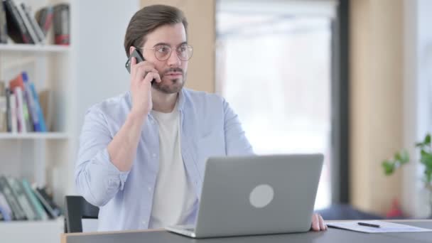 Wütender Mann mit Laptop spricht auf Smartphone — Stockvideo