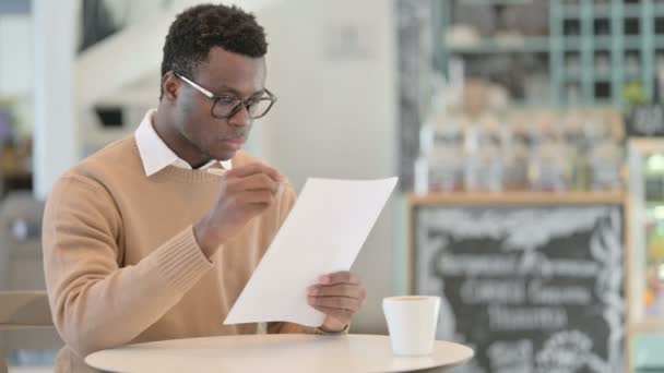 Афроамериканец читает документы, когда пьет кофе в кафе — стоковое видео