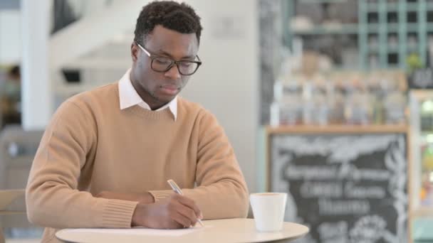 Kafede kahve içerken kağıda yazan Afrikalı Amerikalı adam. — Stok video