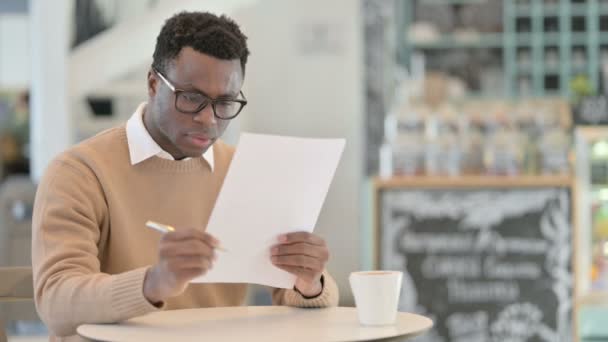 Uomo afroamericano che reagisce alla perdita durante la lettura di documenti in Cafe — Video Stock