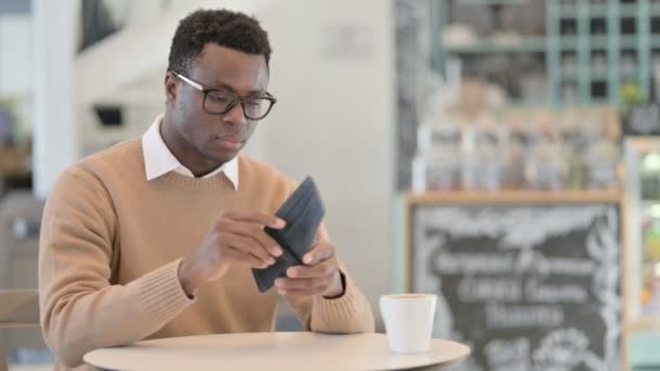Креативний африканський чоловік перевіряє порожній гаманець сидячи в кафе — стокове відео