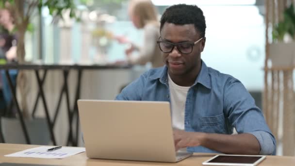 Молодой африканский человек указывает на камеру во время работы над ноутбуком — стоковое видео