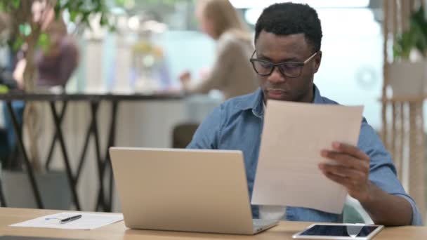 在笔记本电脑上工作时阅读文件的非洲年轻人 — 图库视频影像
